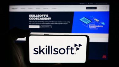 Stuttgart, Almanya - 06-27-2024: ABD 'li e-öğrenim şirketi Skillsoft Corporation' ın logosunun bulunduğu cep telefonu sahibi kişi iş sayfası önünde. Telefon ekranına odaklan.