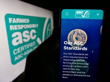 Stuttgart, Almanya - 07-01-2024: Aquaculture Stewardship Council (ASC) organizasyonu web sitesi ile logo önünde akıllı telefon tutan kişi. Telefon ekranının merkezine odaklan.
