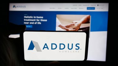 Stuttgart, Almanya - 07-03-2024: ABD 'li ev bakımı şirketi Addus HomeCare Corporation' ın logosuyla cep telefonu sahibi kişi iş sayfası önünde. Telefon ekranına odaklan.