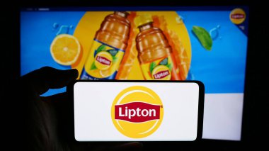 Stuttgart, Almanya - 07-03-2024: İş sayfasının önünde çay markası Lipton logosu taşıyan kişi. Telefon ekranına odaklan.