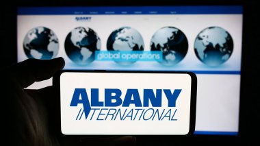 Stuttgart, Germany - 07-03-2024: Person holding cellphone with logo of American industrial goods company Albany International Corp. in front of webpage. Focus on phone display. clipart