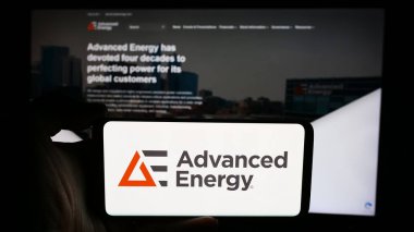 Stuttgart, Germany - 07-03-2024: Person holding cellphone with logo of US technology company Advanced Energy Industries Inc. in front of business webpage. Focus on phone display. clipart