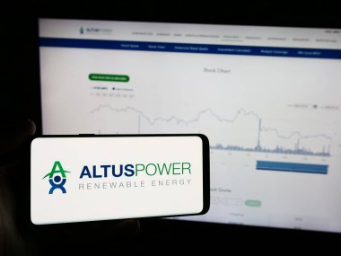 Stuttgart, Germany - 07-03-2024: Person holding mobile phone with logo of American solar energy company Altus Power Inc. in front of business website. Focus on phone display. clipart