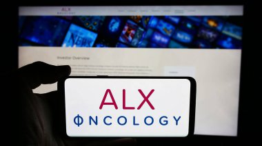 Stuttgart, Almanya - 07-03-2024: ABD 'li kanser terapi şirketi ALX Onkoloji A.Ş.' nin logosuyla cep telefonu sahibi kişi iş sayfasının önünde. Telefon ekranına odaklan.