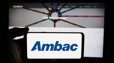 Stuttgart, Almanya - 07-03-2024: Amerikan finans şirketi Ambac Financial Group Inc. 'in logosuyla cep telefonu sahibi kişi iş sayfasının önünde. Telefon ekranına odaklan.
