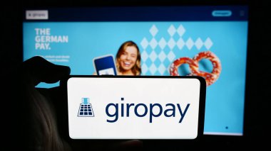 Stuttgart, Almanya - 07-04-2024: İş sayfası önünde Alman ödeme şirketi Giropay 'in (Paydirekt GmbH) logosuyla cep telefonu tutan kişi. Telefon ekranına odaklan.