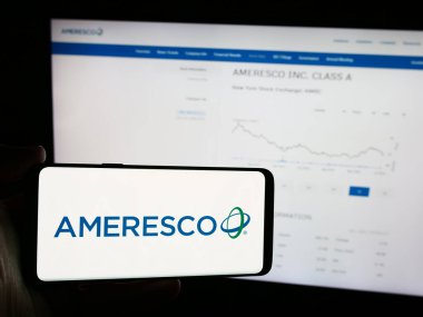 Stuttgart, Germany - 07-05-2024: Person holding mobile phone with logo of American renewable energy company Ameresco Inc. in front of business web page. Focus on phone display. clipart