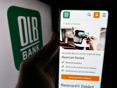 Stuttgart, Almanya - 07-05-2024: Alman Oldenburgische Landesbank AG (OLB) şirketinin logosu önünde cep telefonu tutan kişi. Telefon ekranının merkezine odaklan.