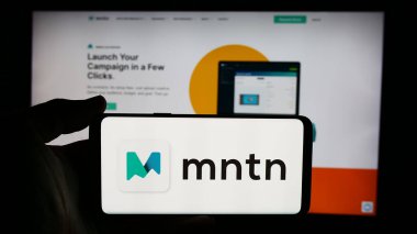 Stuttgart, Almanya - 07-05-2024: ABD 'li reklam yazılım şirketi MNTN Inc.' in logosuyla cep telefonu sahibi kişi iş sayfasının önünde. Telefon ekranına odaklan.
