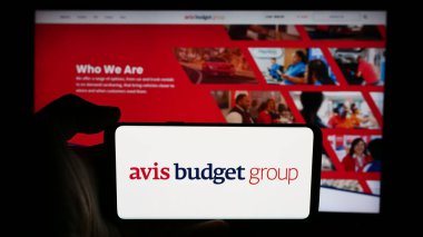 Stuttgart, Almanya - 07-05-2024: ABD 'li kiralık araba şirketi Avis Budget Group Inc.' in logosuyla cep telefonu sahibi kişi iş sayfasının önünde. Telefon ekranına odaklan.