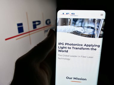 Stuttgart, Almanya - 07-06-2024: ABD 'li lazer şirketi IPG Photonics Corporation' ın web sitesi ile iş logosu önünde cep telefonu tutan kişi. Telefon ekranının merkezine odaklan.
