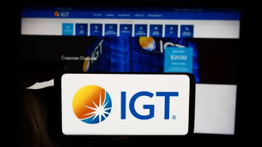 Stuttgart, Almanya - 07-06-2024: International Game Technology plc (IGT) şirketinin logosuna sahip cep telefonu sahibi kişi iş sayfası önünde. Telefon ekranına odaklan.