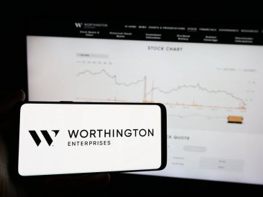 Stuttgart, Almanya - 07-06-2024: Web sayfası önünde üzerinde ABD 'li metal işleme şirketi Worthington Enterprises Inc.' in logosu bulunan cep telefonu sahibi kişi. Telefon ekranına odaklan.