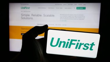Stuttgart, Almanya - 07-06-2024: ABD 'li koruyucu giyim şirketi UniFirst Corporation' ın logosuna sahip akıllı telefon sahibi kişi web sitesi önünde. Telefon ekranına odaklan.