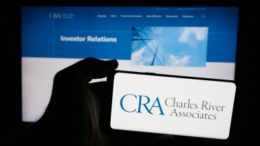 Stuttgart, Germany - 07-06-2024: Person holding smartphone with logo of CRA International Inc. (Charles River Associates) in front of website. Focus on phone display. clipart