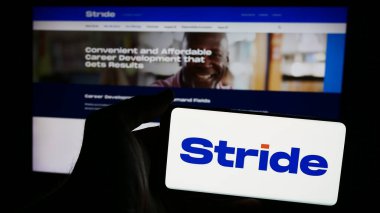 Stuttgart, Germany - 07-08-2024: Person holding smartphone with logo of US online education company Stride Inc. in front of website. Focus on phone display. clipart