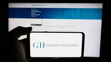 Stuttgart, Almanya - 07-08-2024: ABD 'li medya şirketi Graham Holding Company' nin logosuyla cep telefonu sahibi kişi iş sayfası önünde. Telefon ekranına odaklan.