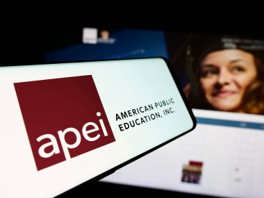 Stuttgart, Germany - 07-08-2024: Person holding smartphone with logo of US company American Public Education Inc. (APEI) in front of website. Focus on phone display. clipart