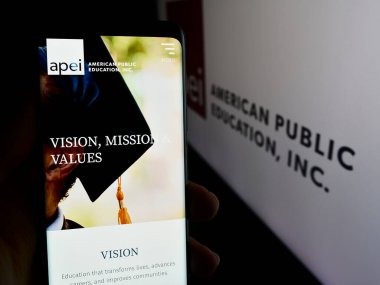 Stuttgart, Almanya - 07-08-2024: ABD 'li Public Education Inc. (APEI) şirketinin logosuna sahip akıllı telefon sahibi kişi web sitesi önünde. Telefon ekranına odaklan.