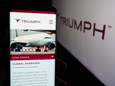 Stuttgart, Almanya - 07-08-2024: Amerikan havacılık şirketi Triumph Group Inc. 'in web sayfası ile iş logosu önünde cep telefonu tutan kişi. Telefon ekranının merkezine odaklan.