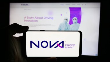 Stuttgart, Almanya - 07-08-2024: İsrailli metroloji şirketi Nova Ltd. 'nin logosuyla cep telefonu tutan kişi iş sayfasının önünde. Telefon ekranına odaklan.