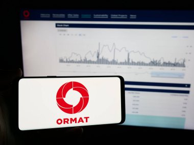 Stuttgart, Almanya - 07-08-2024: Jeotermal enerji şirketi Ormat Technologies Inc. 'nin logosuna sahip cep telefonu sahibi kişi iş sayfasının önünde. Telefon ekranına odaklan.