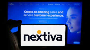 Stuttgart, Almanya - 07-10-2024: ABD 'li iletişim yazılım şirketi Nextiva Inc.' in logosuyla cep telefonu sahibi kişi iş sayfasının önünde. Telefon ekranına odaklan.