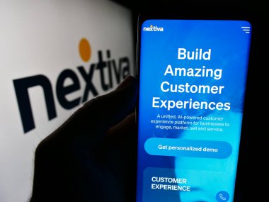 Stuttgart, Almanya - 07-10-2024: ABD 'li iletişim yazılım şirketi Nextiva Inc.' in web sayfası ile logo önünde cep telefonu tutan kişi. Telefon ekranının merkezine odaklan.