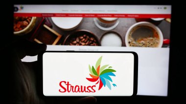Stuttgart, Almanya - 07-10-2024: İsrailli tüketici malları şirketi Strauss Group Ltd. 'nin logosuyla cep telefonu tutan kişi iş sayfasının önünde. Telefon ekranına odaklan.