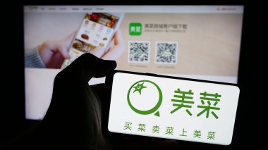 Stuttgart, Almanya - 07-10-2024: Çinli tarım e-ticaret şirketi Meicai 'nin logosunun bulunduğu cep telefonu sahibi kişi iş sayfasının önünde. Telefon ekranına odaklan.