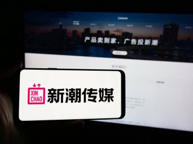 Stuttgart, Almanya - 07-11-2024: Reklam şirketi Chengdu Xinchao Media Group Co. Ltd. nin logosuyla cep telefonu sahibi kişi web sayfasının önünde. Telefon ekranına odaklan.