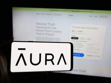 Stuttgart, Almanya - 07-12-2024: İnternet sitesi önünde ABD 'li siber güvenlik yazılım şirketi Aura Sub LLC' nin logosuna sahip kişi. Telefon ekranına odaklan.