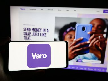 Stuttgart, Almanya - 07-12-2024: Amerikan finans hizmetleri şirketi Varo Bank NA 'nın logosuyla cep telefonu sahibi kişi iş sayfasının önünde. Telefon ekranına odaklan.