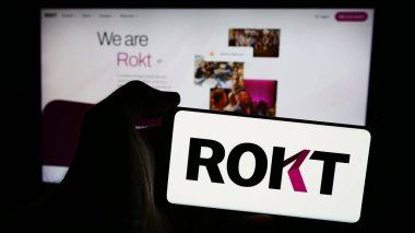 Stuttgart, Almanya - 07-14-2024: E-ticaret teknoloji şirketi Rokt Pte 'nin logosuna sahip cep telefonu sahibi kişi. Ltd. İş sayfasının önünde. Telefon ekranına odaklan.