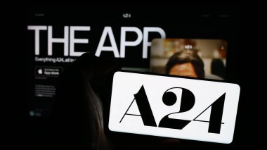 Stuttgart, Germany - 07-14-2024: Person holding mobile phone with logo of American entertainment company A24 Films LLC in front of business web page. Focus on phone display. clipart