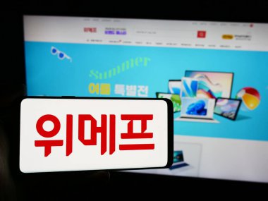 Stuttgart, Germany - 07-14-2024: Person holding smartphone with logo of South Korea e-commerce company Wemakeprice in front of website. Focus on phone display. clipart