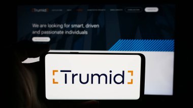 Stuttgart, Almanya - 07-14-2024: ABD 'li fintech şirketi Trumid Holding LLLC' nin logosuna sahip cep telefonu sahibi kişi iş sayfasının önünde. Telefon ekranına odaklan.