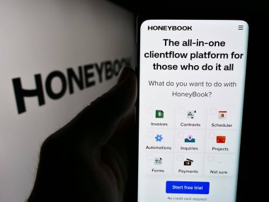 Stuttgart, Almanya - 07-14-2024: ABD 'li müşteri yönetimi şirketi HoneyBook Inc.' in internet sitesiyle logo önünde cep telefonu tutan kişi. Telefon ekranının merkezine odaklan.