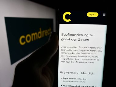 Stuttgart, Almanya - 07-15-2024: Alman finans hizmetleri şirketi Comdirect 'in internet sayfası ile iş logosu önünde cep telefonu tutan kişi. Telefon ekranının merkezine odaklan.