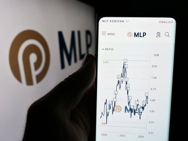 Stuttgart, Almanya - 07-15-2024: Alman finans hizmetleri şirketi MLP SE 'nin web sitesi ile birlikte iş logosu önünde cep telefonu tutan kişi. Telefon ekranının merkezine odaklan.