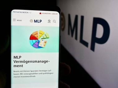 Stuttgart, Almanya - 07-15-2024: Alman finans hizmetleri şirketi MLP SE 'nin web sayfası ile iş logosu önünde akıllı telefon tutan kişi. Telefon ekranının merkezine odaklan.