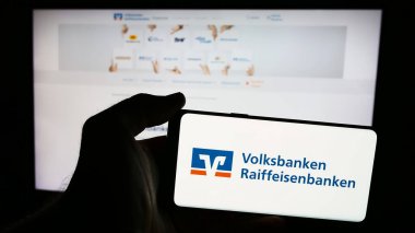 Stuttgart, Almanya - 07-15-2024: Alman bankacılık ağı Volksbanken Raiffeisenbanken 'in logosuna sahip akıllı telefon sahibi kişi web sitesi önünde. Telefon ekranına odaklan.