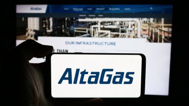Stuttgart, Almanya - 07-16-2024: Kanadalı enerji altyapı şirketi AltaGas Ltd. 'nin logosuyla cep telefonu sahibi kişi iş sayfasının önünde. Telefon ekranına odaklan.