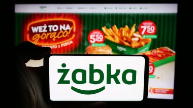 Stuttgart, Almanya - 07-16-2024: Polonyalı perakende şirketi Zabka Polska 'nın logosuna sahip cep telefonu sahibi kişi. - Hoşça kal. İş sayfasının önünde. Telefon ekranına odaklan.