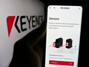 Stuttgart, Almanya - 07-17-2024: Japon elektronik şirketi Keyence Corporation 'ın internet sayfası ile logo önünde cep telefonu tutan kişi. Telefon ekranının merkezine odaklan.