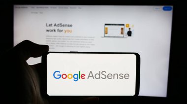 Stuttgart, Almanya - 07-17-2024: İnternet üzerinden reklam programı Google AdSense 'nin logosuna sahip cep telefonu sahibi kişi iş sayfası önünde. Telefon ekranına odaklan.