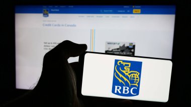 Stuttgart, Germany - 07-17-2024: Person holding cellphone with logo of Canadian financial company Royal Bank of Canada (RBC) in front of business webpage. Focus on phone display. clipart