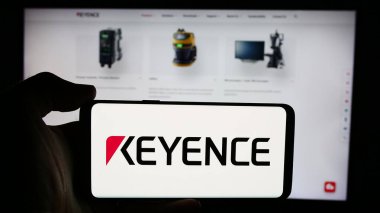 Stuttgart, Almanya - 07-17-2024: Japon elektronik şirketi Keyence Corporation 'ın logosuyla cep telefonu tutan kişi iş sayfasının önünde. Telefon ekranına odaklan.