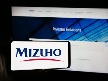 Stuttgart, Almanya - 07-19-2024: Japon bankacılık şirketi Mizuho Financial Group Inc. 'in logosuyla cep telefonu bulunduran kişi web sayfasının önünde. Telefon ekranına odaklan.