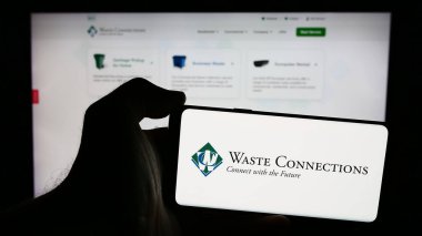 Stuttgart, Germany - 07-19-2024: Person holding smartphone with logo of US recycling company Waste Connections Inc. in front of website. Focus on phone display. clipart